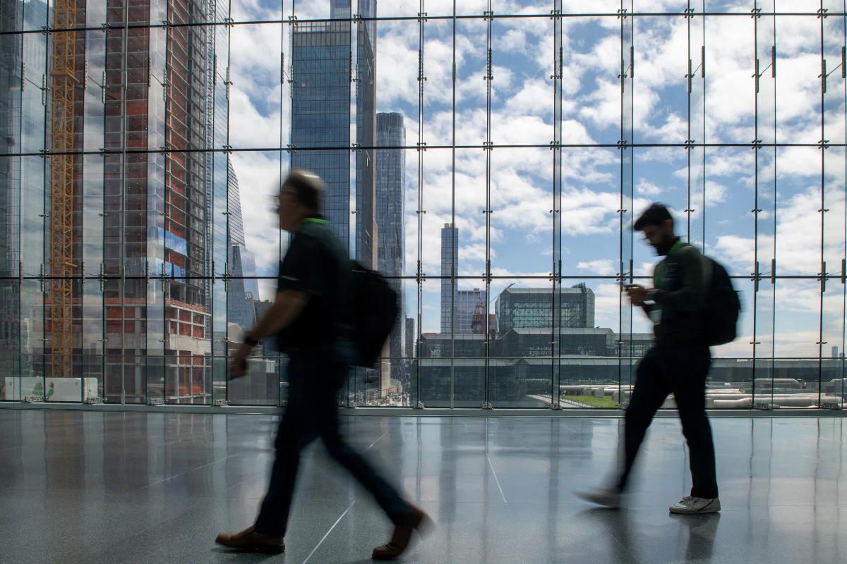 Two attendees walk through a modern glass-walled convention center with a city skyline visible outside.