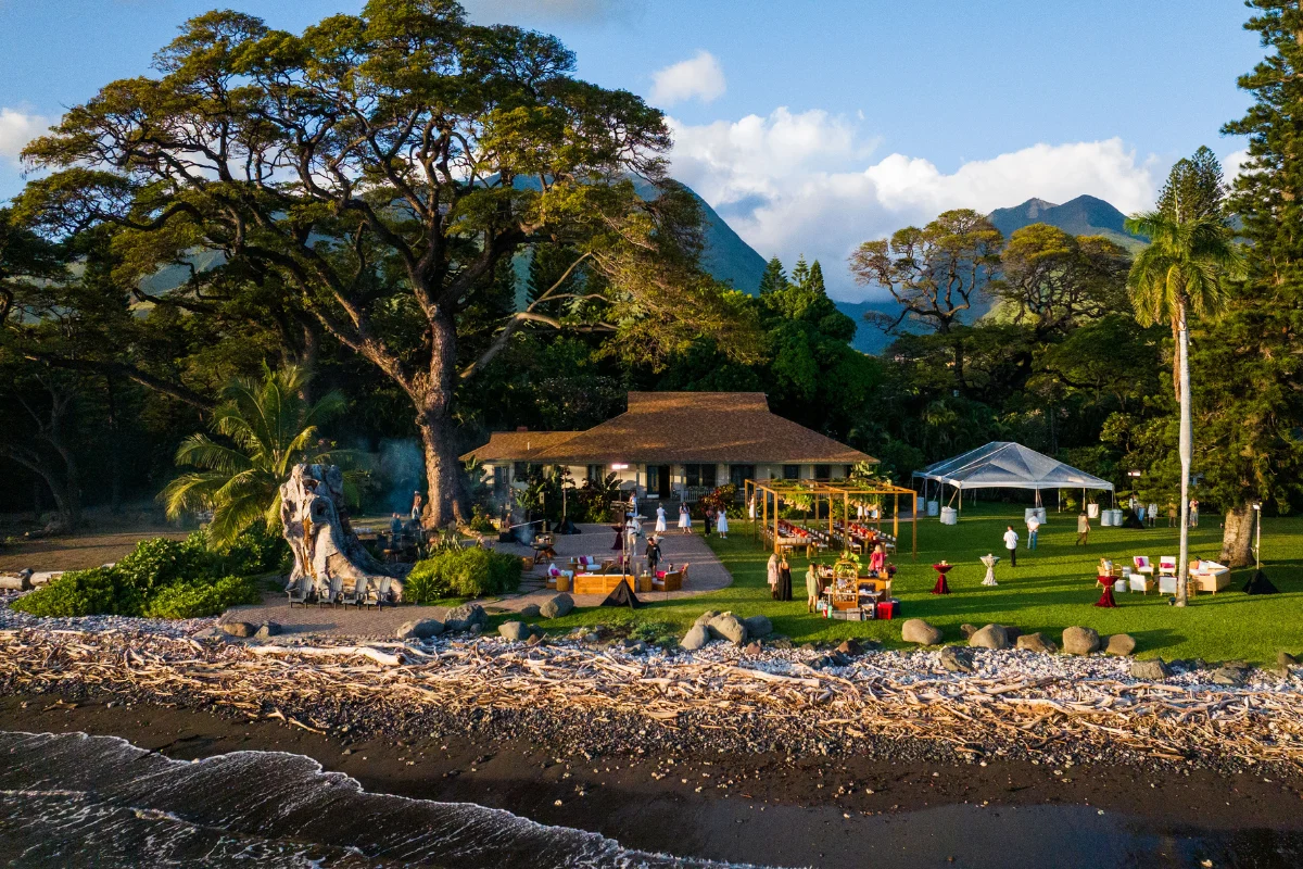 Outdoor event setup on a lush beachfront lawn surrounded by tropical trees and mountains.