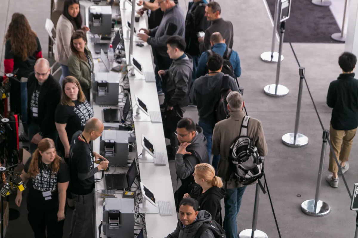 Attendees check in at a busy conference registration area while event staff assist at computer stations.