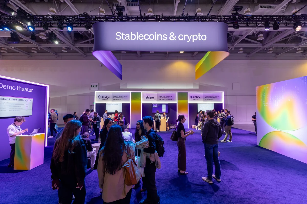 Attendees network and explore colorful exhibitor booths in a conference area focused on stablecoins and cryptocurrency.
